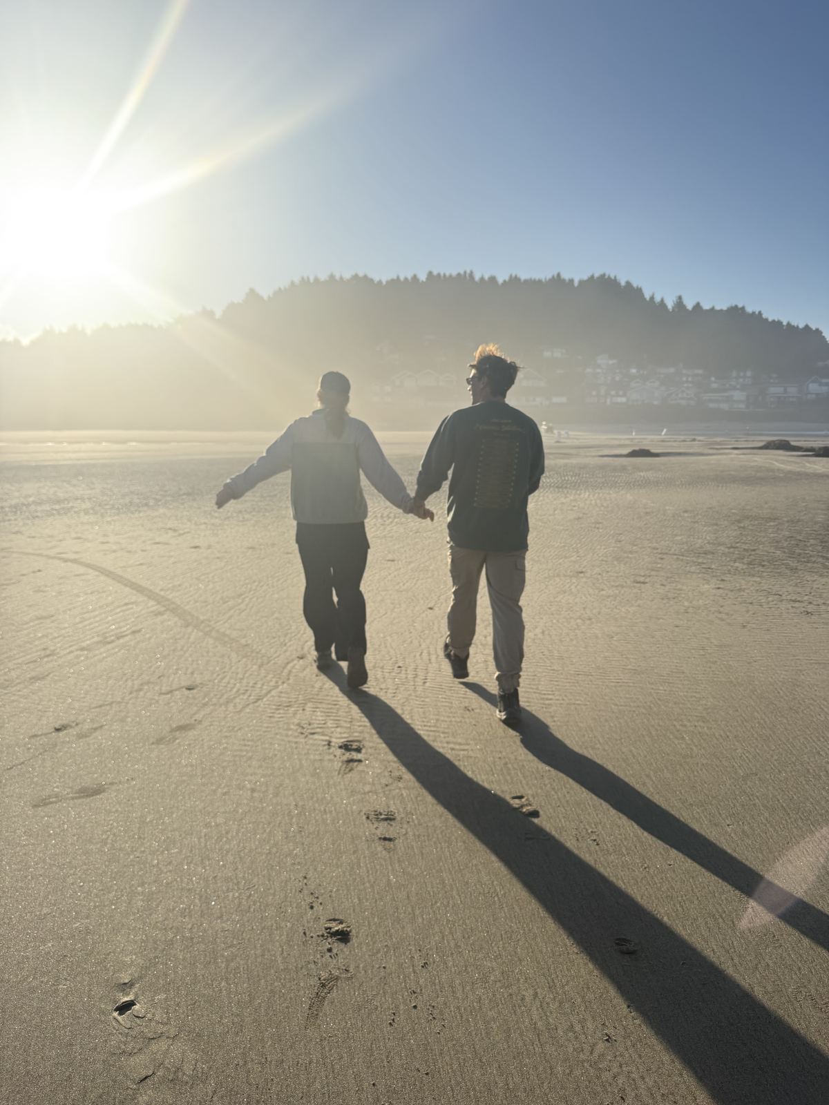The two of us walking hand in hand down a wide beach into low sun