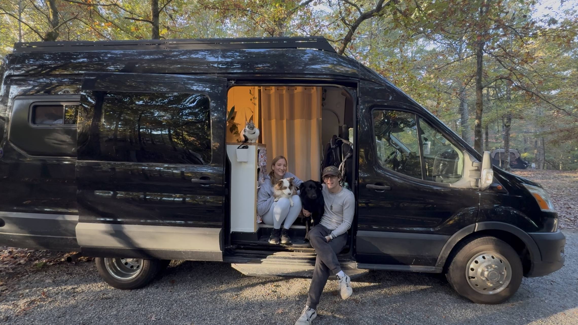 The two of us with the dogs and the cat in the open side door of the van, parked among autumn trees